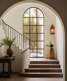 an arched entryway with stairs and potted plants on the table next to it