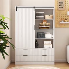 a white cabinet with drawers and shelves in a living room next to a plant on the floor