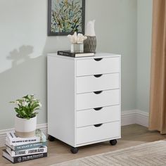 a white chest of drawers in a room with a plant and books on the floor