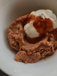 a white bowl filled with ice cream and caramel sauce on top of whipped cream