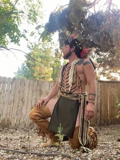 a man dressed in native american garb sitting on the ground next to a fence