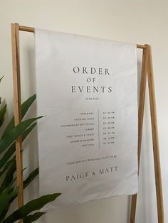 an order of events sign sitting on top of a wooden easel next to a potted plant