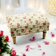 a flower covered foot stool sitting on top of a table next to flowers and candles