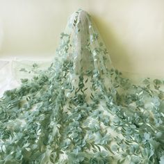 a white and green dress with flowers on it's neckline, draped over by a sheer fabric