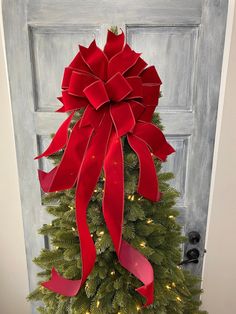 a christmas tree with red bows on it in front of a door decorated for the holiday season