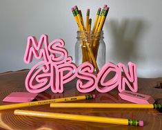 some pencils and markers are sitting on a table next to a glass jar with the word ms gibson written in it