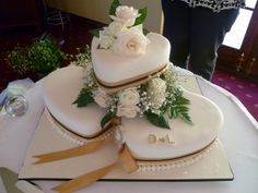 two tiered wedding cake with white flowers and gold ribbon on top, sitting on a table