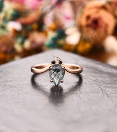 an engagement ring with a pear shaped green stone in the center on top of a wooden table