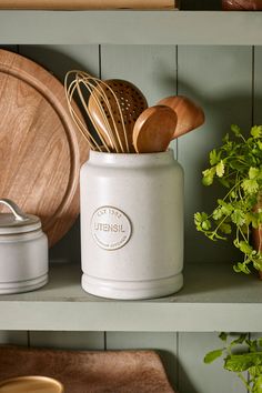 kitchen utensils and wooden spoons in a white ceramic container on a shelf