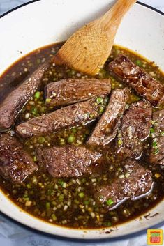 a wooden spoon in a bowl filled with meat and sauce