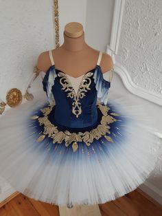 a blue and white tutu with gold accents on the bottom is sitting on a mannequin