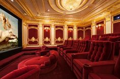 an empty theater with red seats in front of a large screen and paintings on the walls