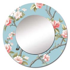 a round mirror with pink flowers on it and a bird perched on the branch, in front of a blue background