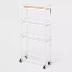 a white rolling cart with three shelves and wheels on the bottom shelf is shown in front of a white background