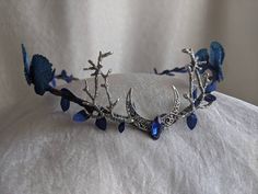 An ethereal woodland tiara featuring sapphire blue leaves (including large blue leaves) surrounding the piece and a moon charm with crystal in the center and two branches at its side. Perfect for special occasions or to add a bit of magic to your every day! The secondary color refers to the metal (silver pictured). Ocean Tiara, Woodland Tiara, Moon Tiara, Crown Aesthetic, Magical Accessories, Headpiece Jewelry, Magical Jewelry, Head Piece, Fantasy Dress