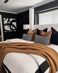 a bedroom with black walls and white bedding, brown throw pillows and blankets on the headboard