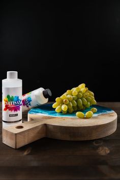 a bottle of paint next to some grapes on a cutting board with a wooden paddle