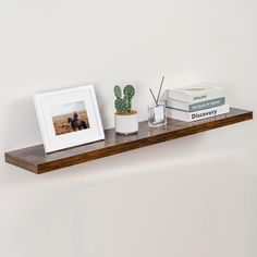 a shelf with two books and a cactus on it next to a framed photo in a white vase