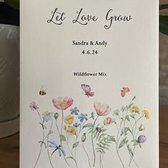 a wedding card with flowers and butterflies on it, sitting next to a potted plant