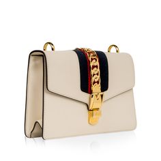 The Gucci Sylvie became an instant classic the moment it landed in stores. The cream hue is complimented by the brand's signature red and blue striped ribbon handle and also features a removable leather shoulder strap ideal for cross-body usage. This stunning bag is an absolutely necessary addition to any luxury handbag collection. With a gold buckle chain prominently depicted on the front flap, the Sylvie is luxurious, glamorous and the perfect compliment to anything you may have in your wardrobe. Whether you dress the Sylvie up or down, you can be sure this eye-catching piece is the ideal accessory for any occasion. Sleek, stylish, sophisticated, but youthful and playful at the same time, the Sylvie is a true must-have. SPL Exterior Smooth cream leather Gold toned hardware Chain buckle d Gucci Sylvie, Handbag Collection, Striped Ribbon, Hand Ring, The Cream, Red Fabric, Exclusive Bag, Handbag Backpack, New Bag