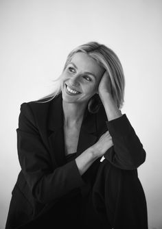 a black and white photo of a smiling woman with her hand on her head, looking at the camera