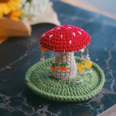 a small crocheted mushroom on top of a green plate with earrings hanging from it