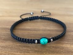 a black cord bracelet with a turquoise bead