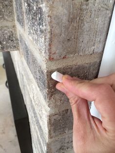 a hand is pointing at the corner of a brick wall that has been painted white