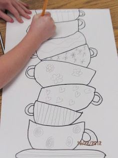 a child's hand writing on a piece of paper with cups and saucers