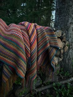 a blanket draped over a pile of logs in front of a tree with the woods behind it