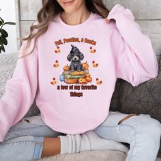 a woman sitting on a couch wearing a pink shirt with an image of a poodle and pumpkins