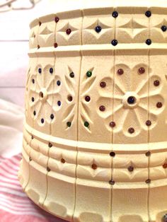 a close up of a white vase with beads on it's sides and a red striped table cloth in the background