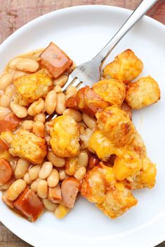 a white plate topped with beans and tater tots next to a silver fork