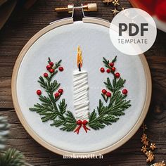 a cross stitch christmas wreath with a lit candle in the center and red berries around it