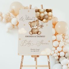 a welcome sign for a baby shower with balloons in the air and a teddy bear on it