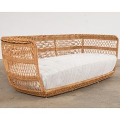 a wicker couch with white cushions on concrete