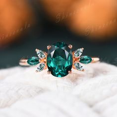 an emerald colored ring with green leaves on the side and two white diamonds in the middle