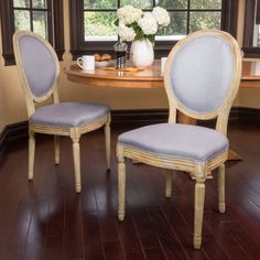 two chairs sitting in front of a table with white flowers on it and a vase