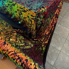 a table covered with a multicolored cloth on top of a tiled floor next to a wall