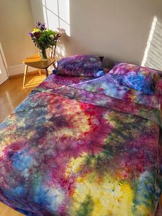 a bed covered in a colorful comforter next to a vase with flowers on it