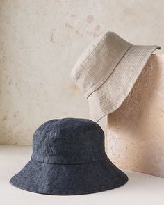 two hats sitting next to each other on top of a white table with a wall in the background