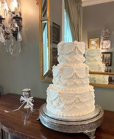 a large white wedding cake sitting on top of a wooden table next to a mirror