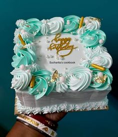 a birthday cake with white frosting and blue icing on the top is being held by a woman