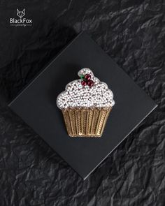 a gold and white cupcake brooch with a red jewel on it's side