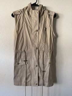 "Vintage Zenana Outfitters Sleeveless Utility Coat This item is brand new in perfect condition. Tag on item reads size \"S\". Please see item measurements listed below. 100% Cotton.  Safari Vibes! Beige sleeveless coat with two big fully functional snap closure pockets on front of garment. Zipper pocket on left chest side is decorative. Snap and zipper main closure. Tie on waste so you can cinch the garment for a more fitted look. Two snap military style shoulder tabs (decorative). Hood is rounded on top. Item Measurements (Garment Lying Flat) Shoulder - 16\" Bust - (Armpit to Armpit) 17\" Waist - 16\" Hem Width - 18\" Length - 27.5\" (Shoulder to Hem) Length - 37\" (Hood to Hem Hood Width - 12\" Hood Length - 10\" Item Care Dry Clean Only Made in Vietnam 🇻🇳  Item Condition Perfect Condi Decorative Hood, Sleeveless Coat, Safari Style, Military Style, Look Plus, Military Fashion, That Look, Shirt Dress, Jackets For Women