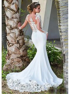 a woman standing next to a palm tree wearing a wedding dress with long sleeves and open back