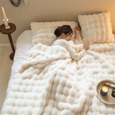 a woman laying in bed under a fluffy white blanket with two candles on the side