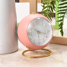 a pink and white clock sitting on top of a table next to a potted plant