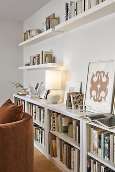 a living room filled with lots of books on top of a white book shelf next to a brown chair