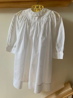 White cotton dobby dress with 3/4 sleeves, smock styling, and lace-collared neck with mother-of-pearl buttons at the back. 2 1/2" turned hem. Fabric had worn through in a couple of spots due to age, one 1/16" shown in last photo. Because these are lost in the folds of the dress I have left them. Dress is priced accordingly; it has no labels.  Dimensions: 8" across at shoulders 22 1/2" garment length shoulder to hem 12 1/2" sleeve length Cotton Bishop Sleeve Daywear Dress, Cotton Bishop Sleeve Dresses For Daywear, Classic Cotton Prairie Dress For Daywear, Cotton Peasant Dress For Daywear, Classic Daywear Dresses With Smocked Back, Classic Dresses With Smocked Back For Daywear, Cotton Half Sleeve Blouse For Daywear, Peasant Dresses With Smocked Cuffs For Daywear, Classic Cotton Dress With Lace Collar